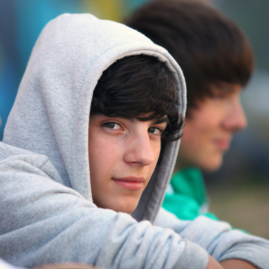 A teenager smiling at the camera wearing a grey hoodie with the hood up